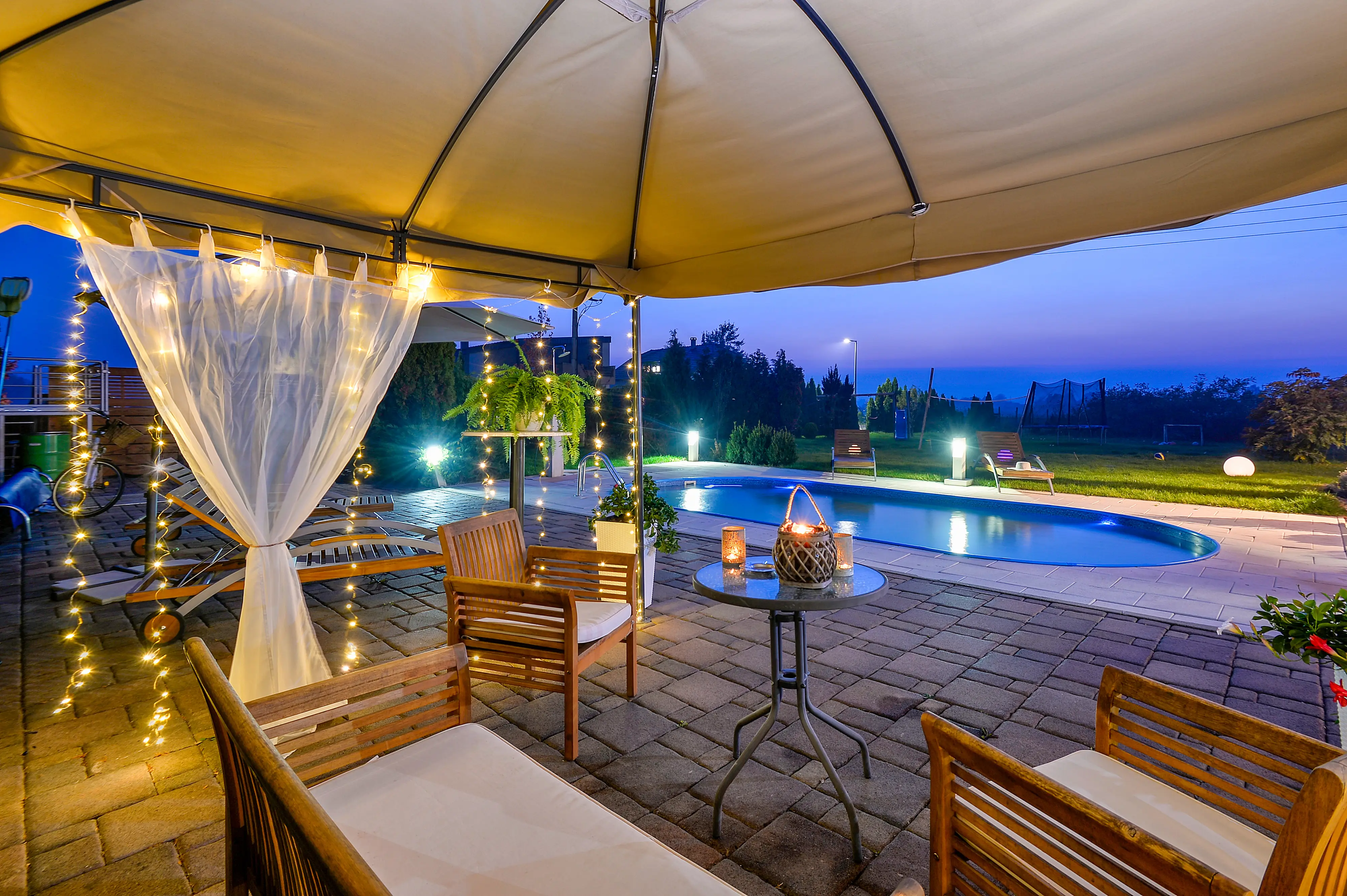 Evening patio table beside lit pool and gazebo