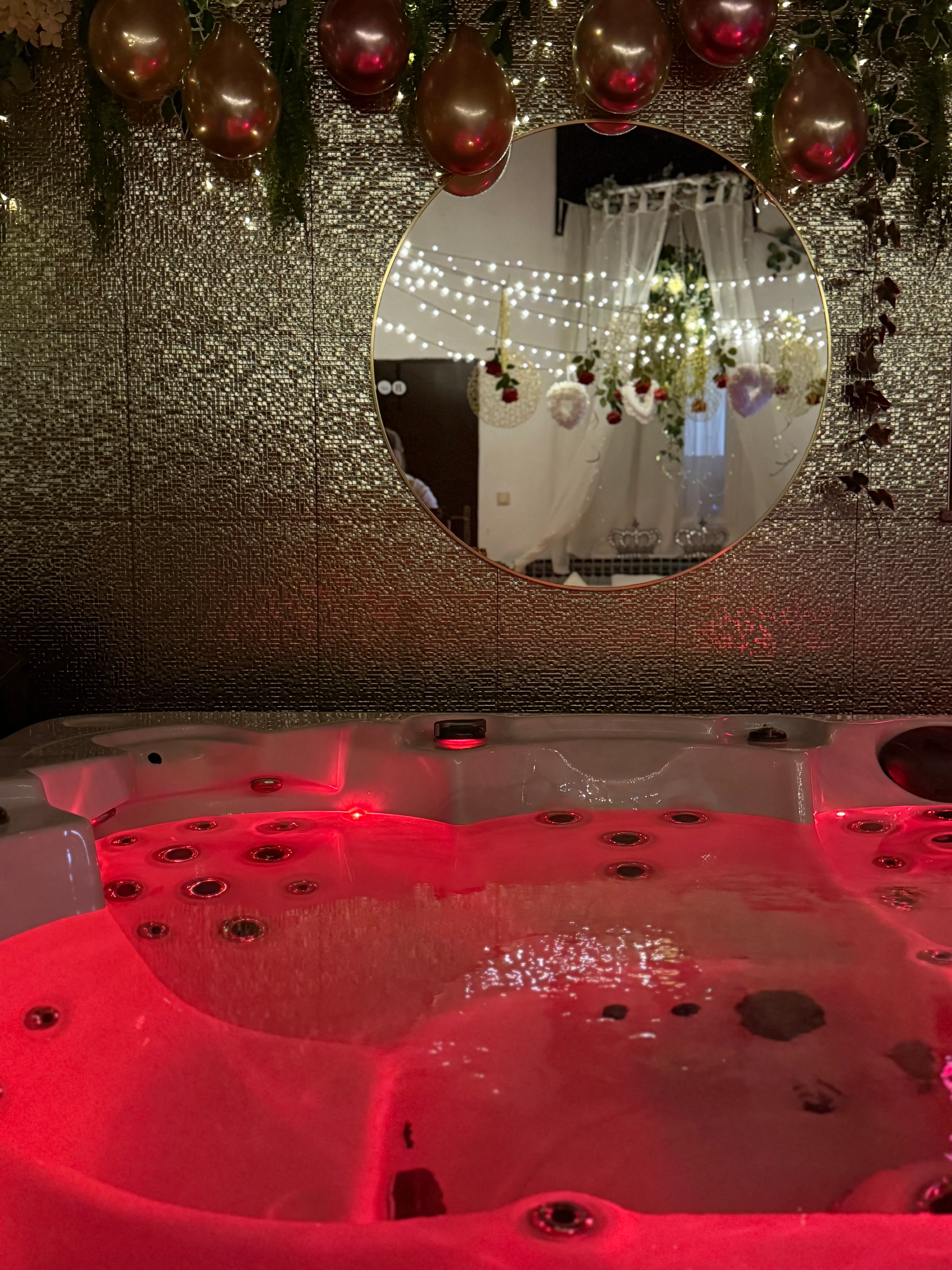 Red-lit jacuzzi under round mirror and metallic wall