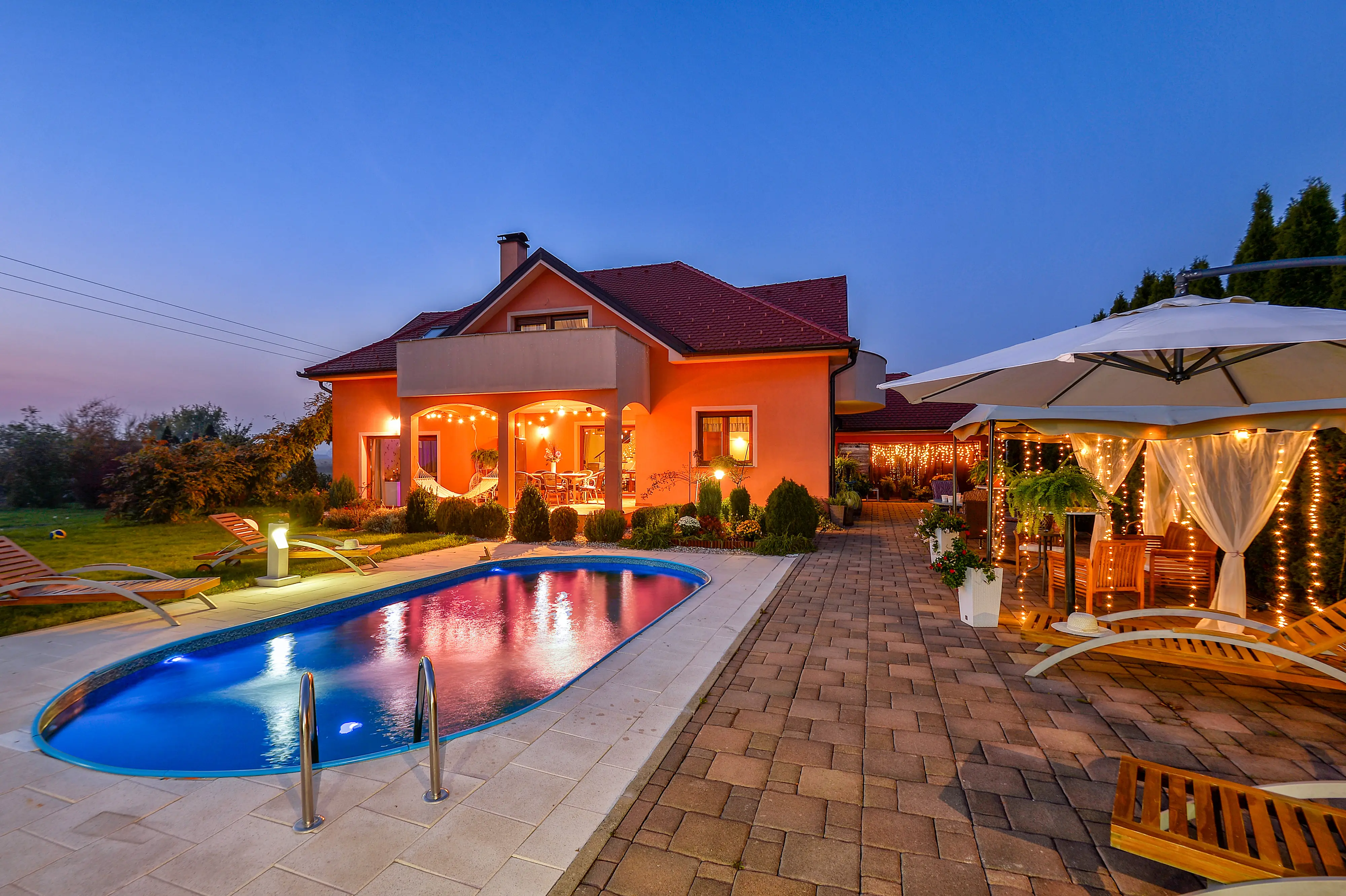 Twilight exterior with lit pool and warm house lighting